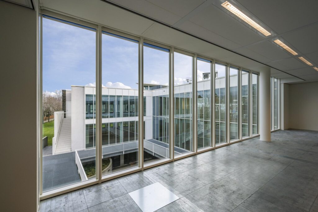 Uitzicht vanuit een leeg kantoor op de moderne glazen gevel van een gebouw aan de De Cuserstraat.